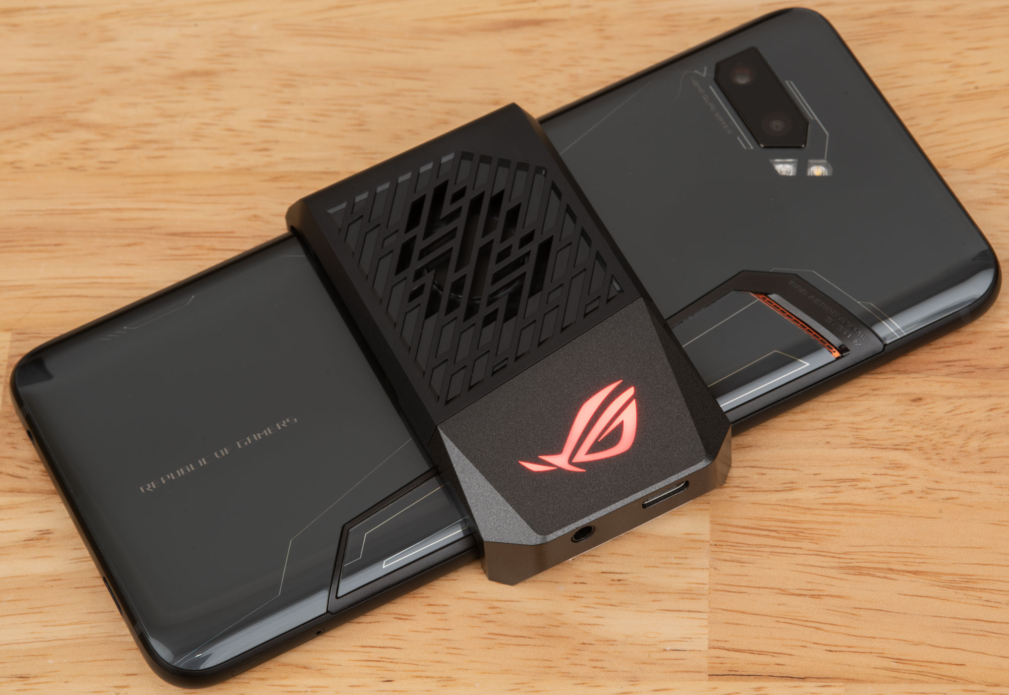  A black Asus ROG Phone 8 Series smartphone with a black ROG Phone 8 Series AeroActive Cooler with red light up logo attached to the back.